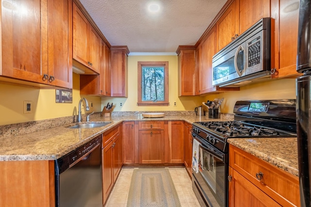 kitchen with a sink, brown cabinets, black appliances, and light stone countertops