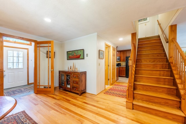 entryway with a textured ceiling, stairs, and light wood-style flooring
