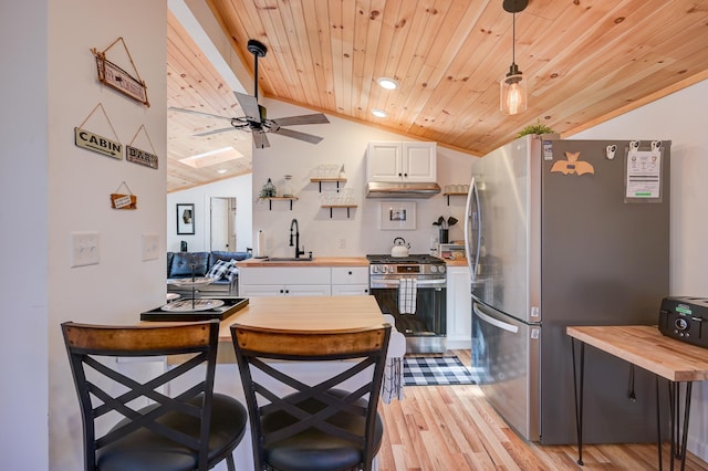 kitchen featuring wooden counters, vaulted ceiling, a sink, under cabinet range hood, and stainless steel appliances
