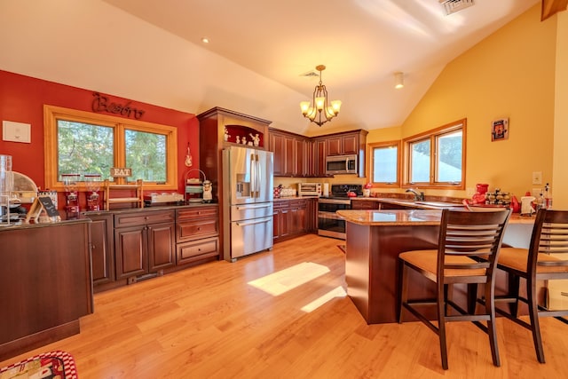 kitchen featuring appliances with stainless steel finishes, a chandelier, light wood-style flooring, a peninsula, and vaulted ceiling