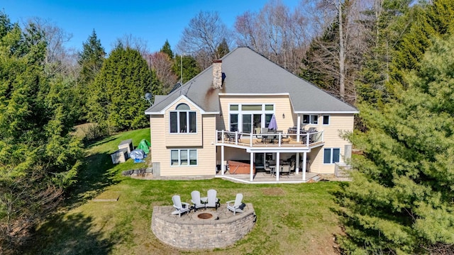 rear view of house featuring a hot tub, an outdoor fire pit, a wooden deck, a patio area, and a lawn