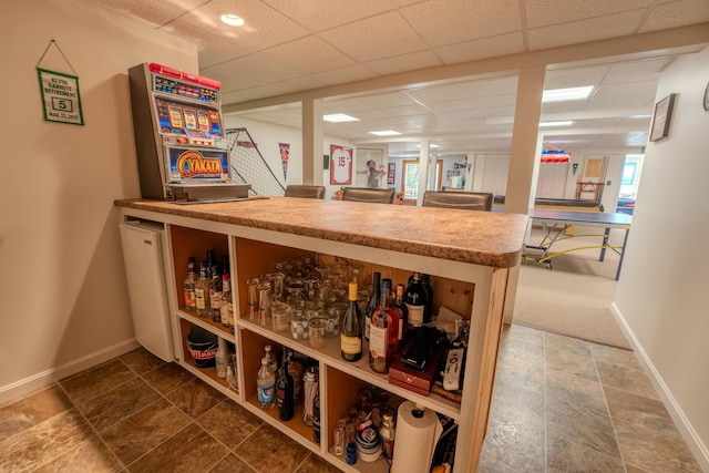 bar with baseboards, a paneled ceiling, and stone finish floor