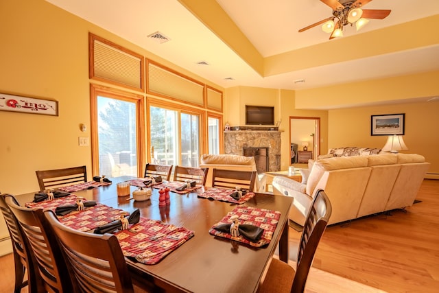 dining room with ceiling fan, a fireplace, wood finished floors, and visible vents