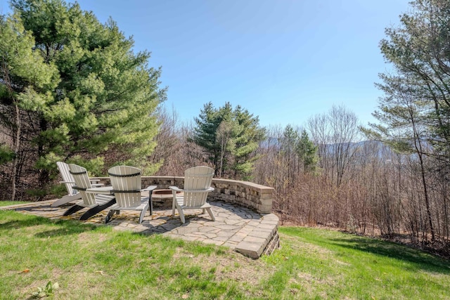 view of yard featuring a wooded view, a patio area, and an outdoor fire pit