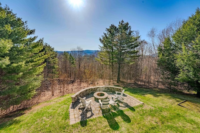 view of yard featuring a view of trees, a patio area, and an outdoor fire pit