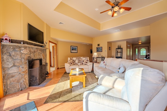 living room featuring a stone fireplace, a baseboard radiator, ceiling fan, and light wood-type flooring