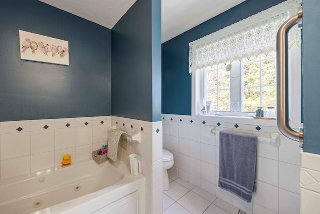 bathroom with a jetted tub, tile walls, tile patterned flooring, wainscoting, and toilet