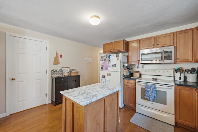 kitchen featuring white appliances, brown cabinetry, light wood finished floors, and a center island