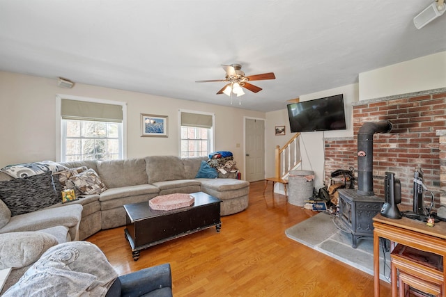 living area with stairway, a wood stove, a ceiling fan, and light wood finished floors