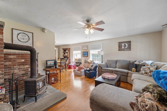 living room with a wood stove, a ceiling fan, and wood finished floors