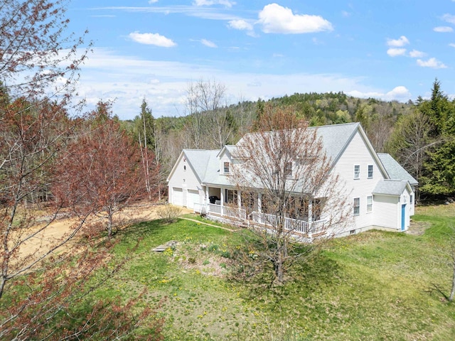back of property with an attached garage, a shingled roof, a porch, a yard, and a wooded view