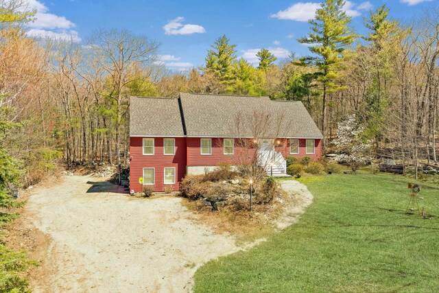 view of front of home featuring roof with shingles, driveway, and a front yard