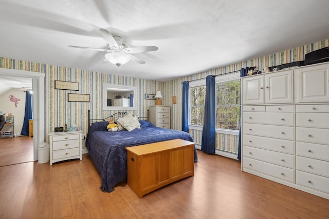 bedroom with light wood-type flooring, a ceiling fan, and wallpapered walls