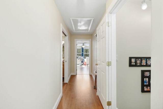 corridor with light wood-type flooring, attic access, and baseboards