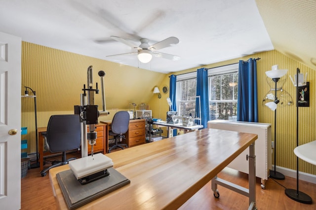 home office featuring a ceiling fan, wallpapered walls, wood finished floors, and lofted ceiling