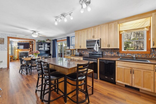 kitchen with light brown cabinetry, stainless steel appliances, dark countertops, and a sink