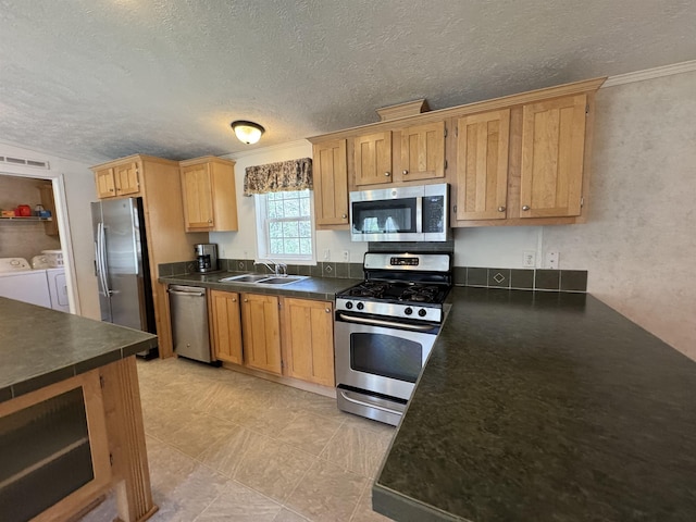 kitchen featuring a sink, appliances with stainless steel finishes, dark countertops, and washer and dryer