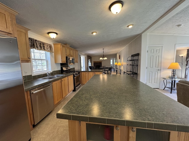 kitchen featuring a textured ceiling, appliances with stainless steel finishes, a center island, dark countertops, and a sink