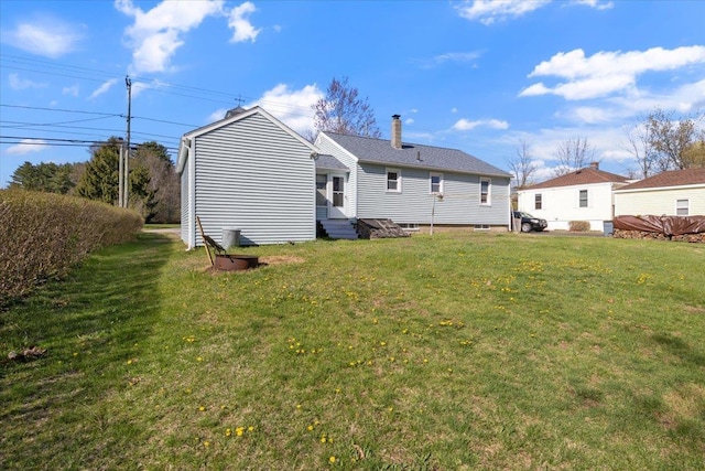 rear view of house with entry steps, a chimney, and a yard