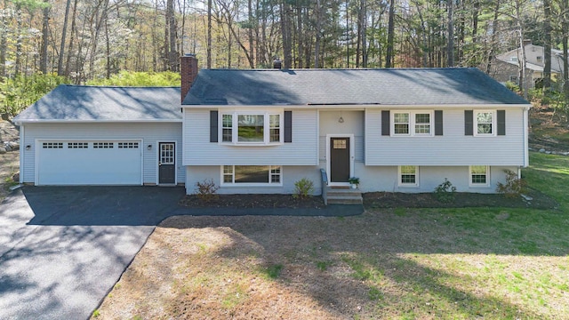 split foyer home with a front lawn, a chimney, entry steps, an attached garage, and driveway