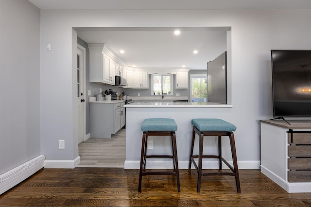 kitchen with a kitchen breakfast bar, wood finished floors, white cabinets, a baseboard heating unit, and a peninsula