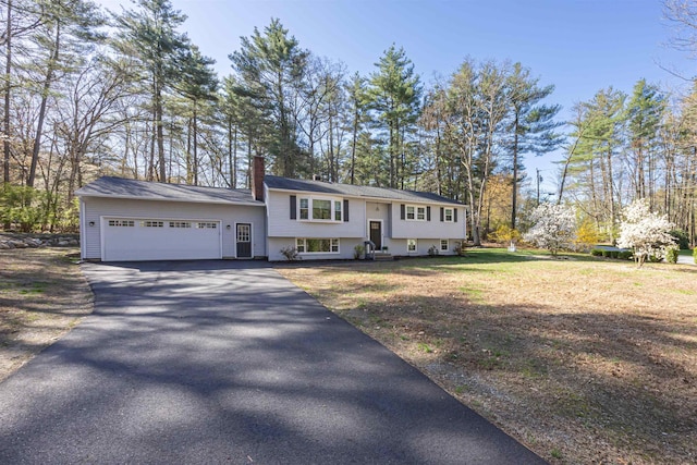 raised ranch with a garage, a chimney, and aphalt driveway