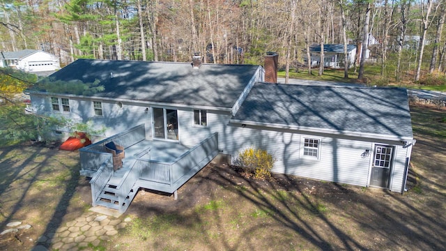 rear view of property with a deck, a chimney, and a shingled roof