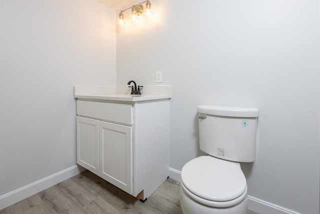 half bath with baseboards, wood finished floors, toilet, and vanity