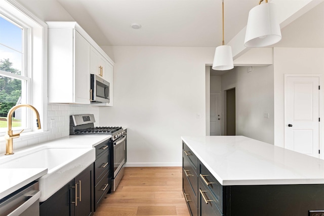 kitchen with a kitchen island, a sink, light wood-style flooring, appliances with stainless steel finishes, and backsplash
