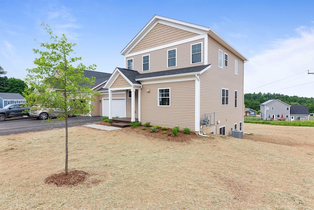 traditional home featuring a garage, central air condition unit, and aphalt driveway