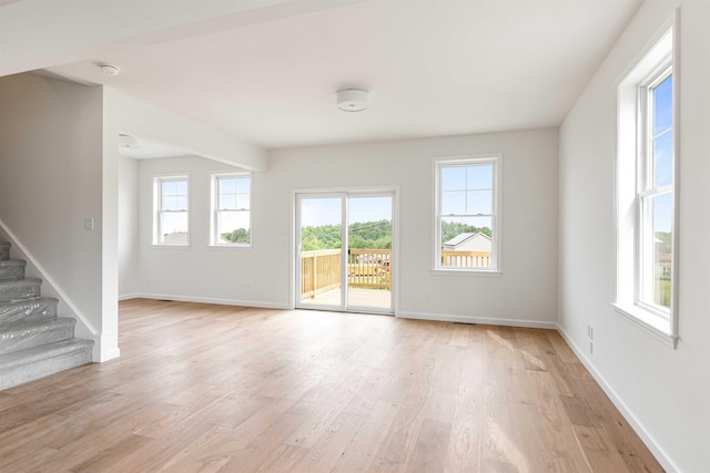 unfurnished living room featuring stairway, baseboards, and light wood finished floors