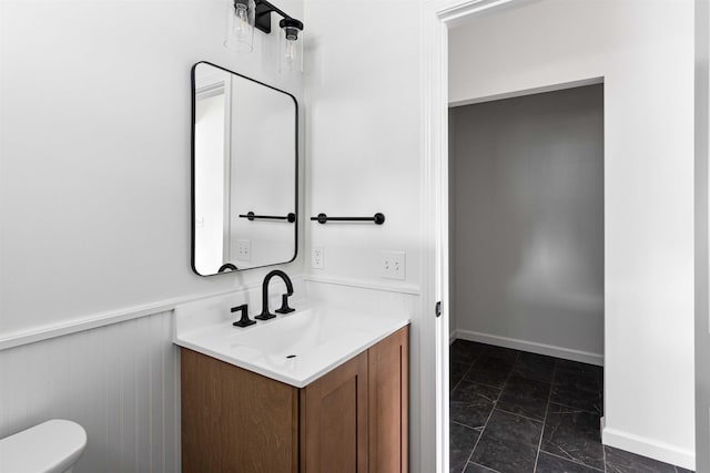 half bathroom featuring toilet, baseboards, marble finish floor, and vanity