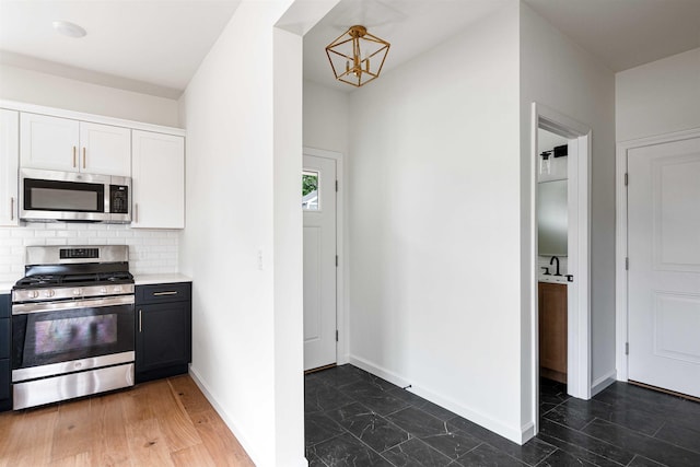 kitchen with white cabinets, light countertops, a chandelier, stainless steel appliances, and baseboards