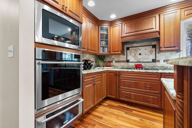 kitchen with decorative backsplash, light stone countertops, stainless steel appliances, and light wood-style flooring