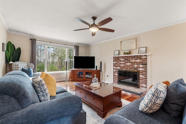 living room featuring crown molding, ceiling fan, a brick fireplace, and light wood-style flooring