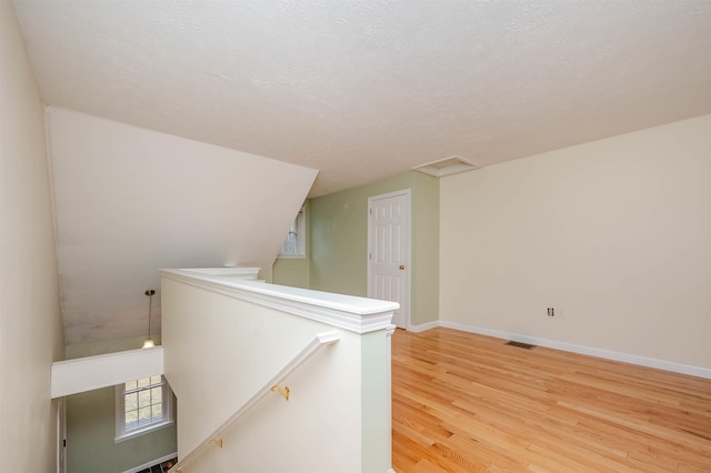 interior space with a textured ceiling, visible vents, baseboards, an upstairs landing, and light wood-style floors