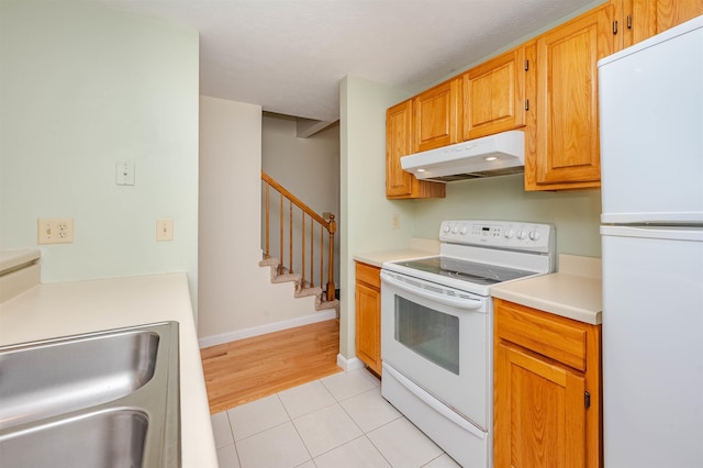 kitchen featuring a sink, white appliances, light countertops, light tile patterned floors, and under cabinet range hood