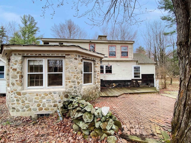 back of house with a wooden deck, a chimney, and stone siding