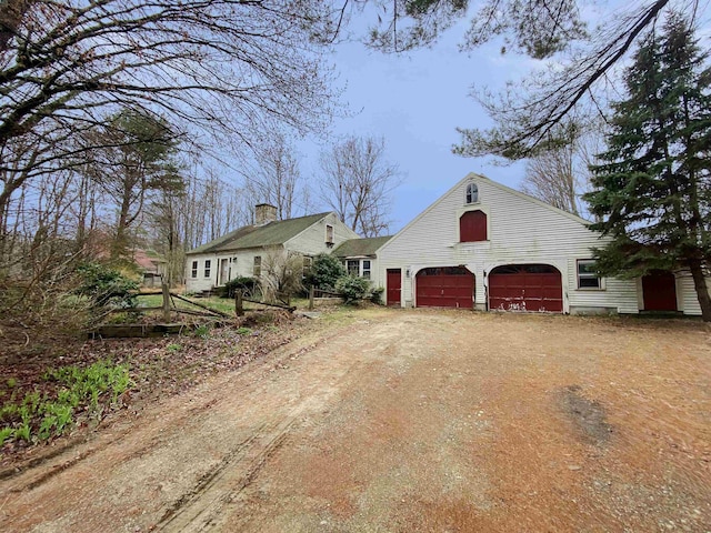 view of side of home featuring a garage, a chimney, and dirt driveway