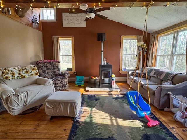 living area with ceiling fan, a wood stove, wood-type flooring, vaulted ceiling, and a baseboard heating unit