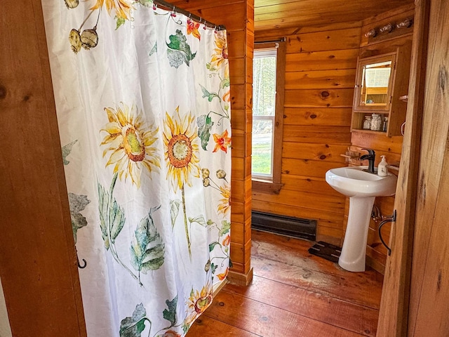 full bath featuring a shower with shower curtain, a baseboard heating unit, a wealth of natural light, and hardwood / wood-style flooring