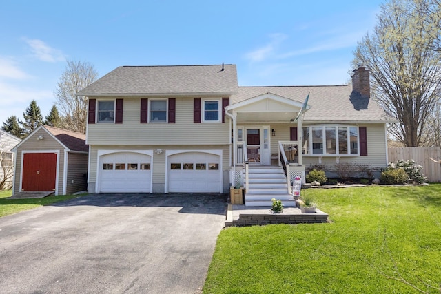 split level home featuring fence, a garage, a front yard, a chimney, and driveway