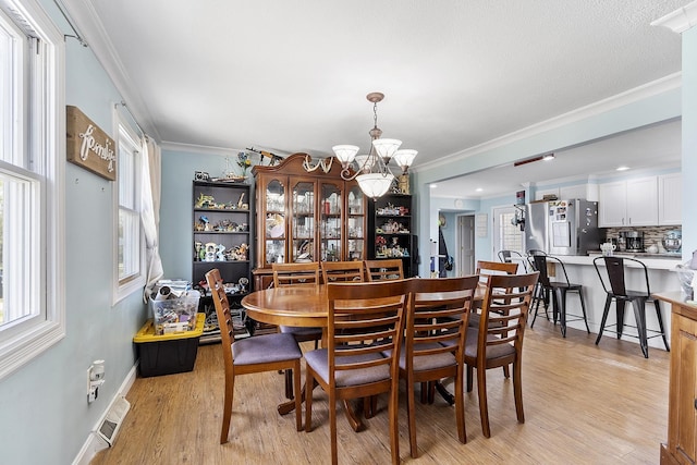 dining space with light wood-type flooring, ornamental molding, a chandelier, and a healthy amount of sunlight