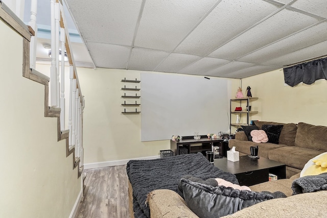 living area with stairway, baseboards, wood finished floors, and a paneled ceiling