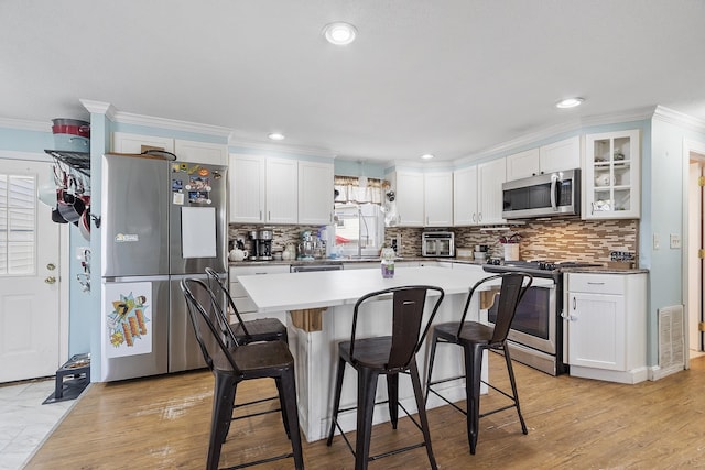 kitchen with decorative backsplash, white cabinetry, appliances with stainless steel finishes, and a kitchen breakfast bar