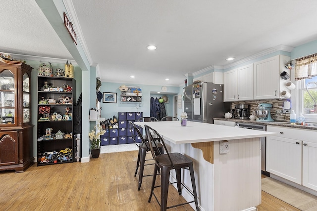 kitchen with a kitchen island, light wood-style floors, a kitchen breakfast bar, white cabinetry, and appliances with stainless steel finishes