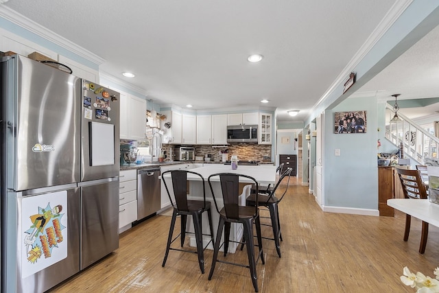 kitchen with ornamental molding, a breakfast bar, white cabinets, appliances with stainless steel finishes, and backsplash