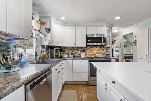 kitchen featuring ornamental molding, wood finished floors, white cabinetry, tasteful backsplash, and appliances with stainless steel finishes