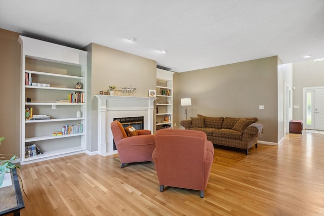 living room featuring baseboards, a glass covered fireplace, built in features, and light wood-type flooring