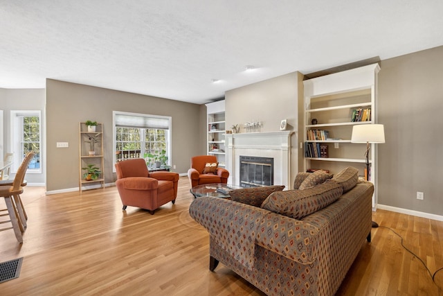 living area with visible vents, built in features, baseboards, light wood-type flooring, and a premium fireplace